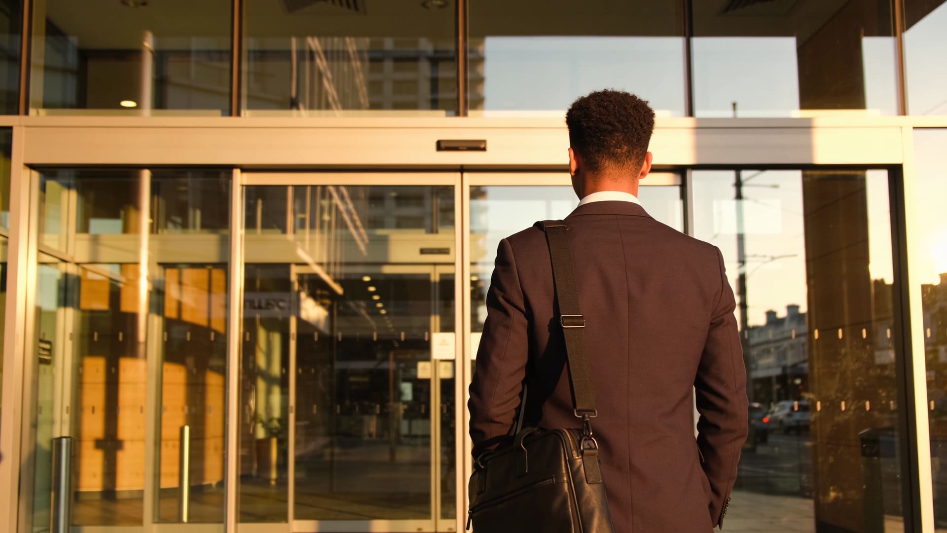 Young professional pausing at the entrance of a modern New Zealand office building in warm morning light, about to walk in for their first day