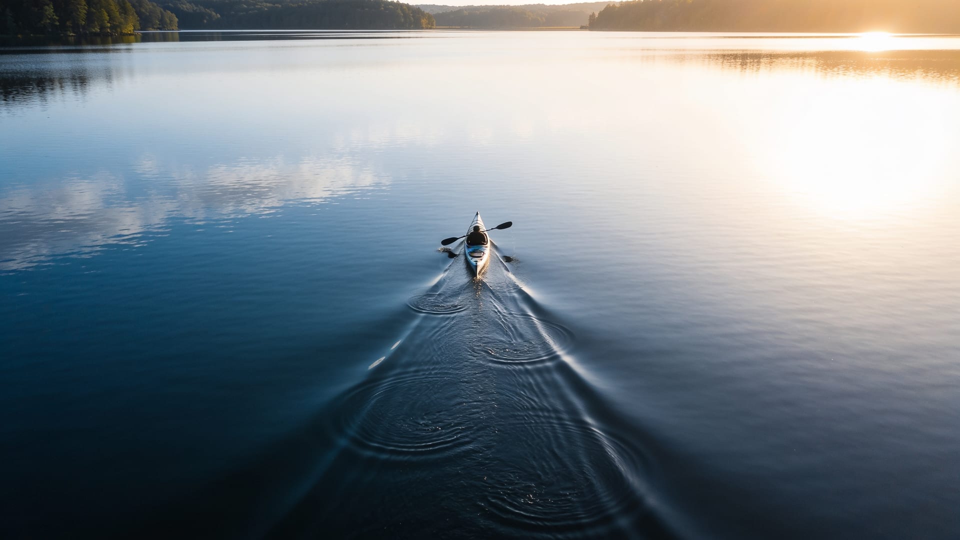 Single kayak cutting a deliberate straight line across a calm New Zealand lake at dawn, one clear direction rather than drifting