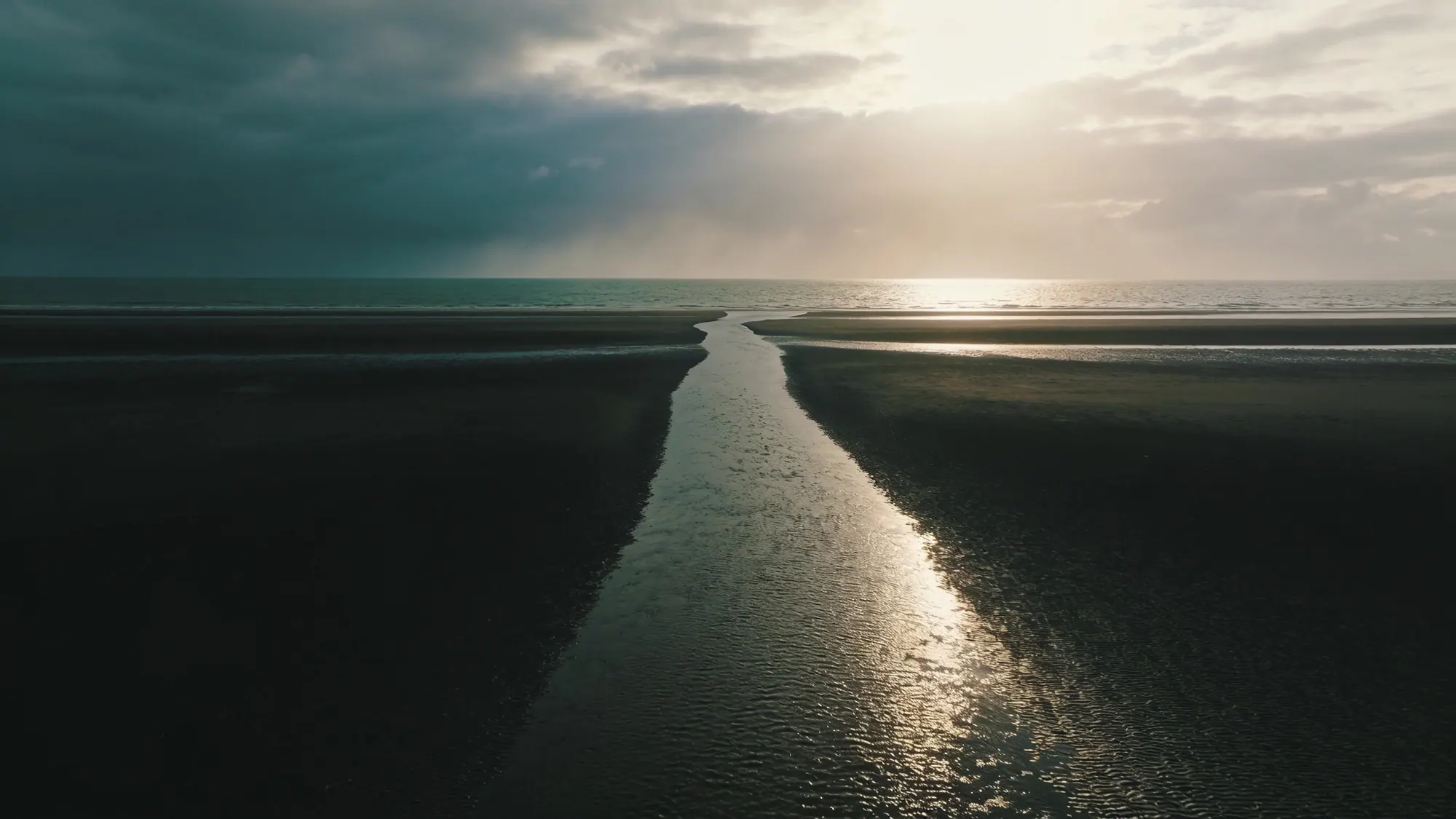 A single tidal channel cutting through a black-sand beach out to the open sea